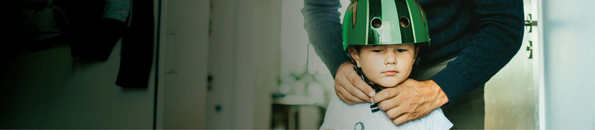 father fastens the strap of green color helmet around his son's head while the son observes
