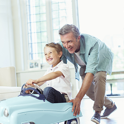 dad feels happy after insuring his son's education and pushes toy car while the son sits on it