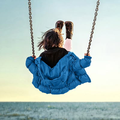 little girl wearing blue jacket and swinging on swing