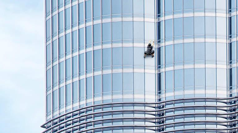 man climbing skyscraper building and holding onto the rail