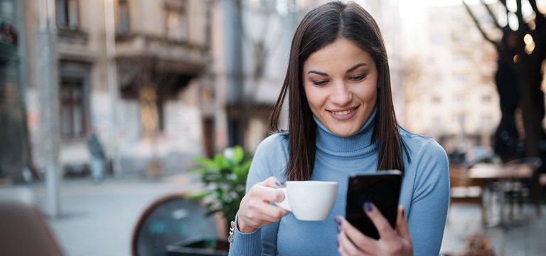 woman seem happy enjoying her coffee and looking at her savings after signing up for sc personal banking using her mobile phone