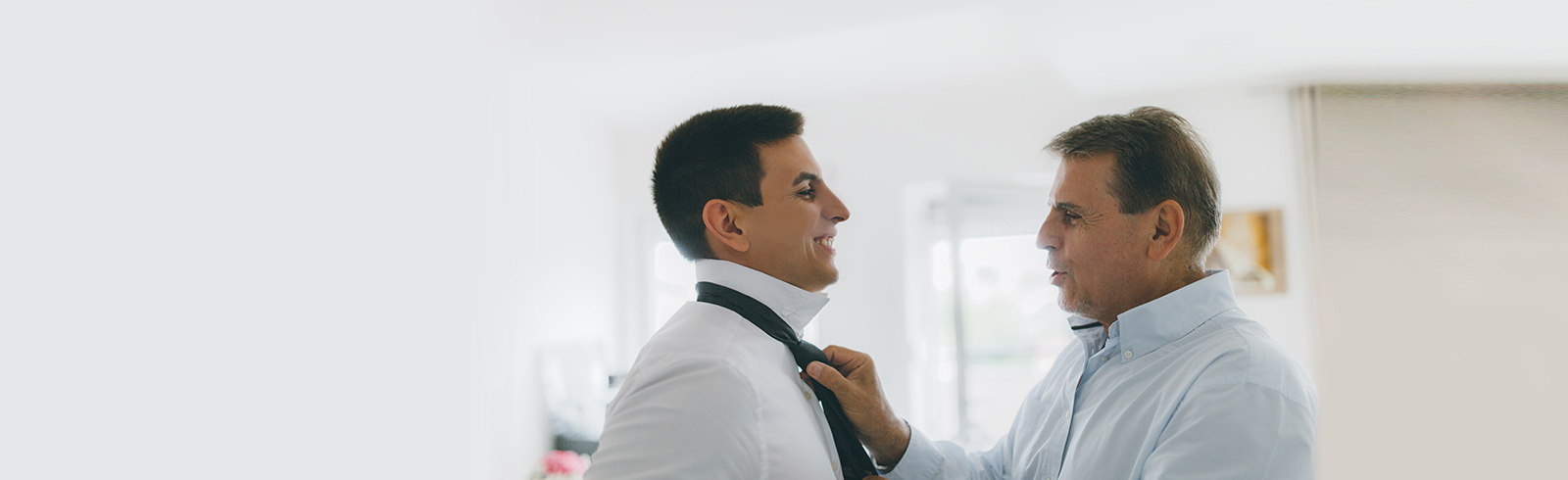 elder father proudly adjusting his son's tie as they both look happy and smiling at each other