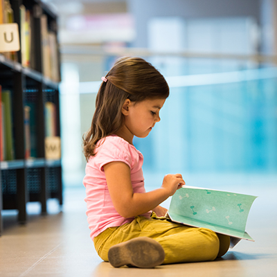 young girl sitting on the library floor and reading her book