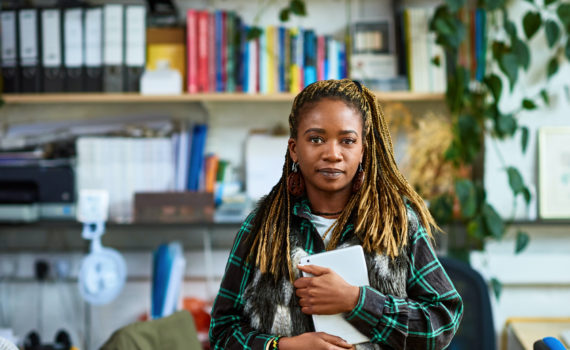 Woman with dreadlocks standing in office, looking at camera