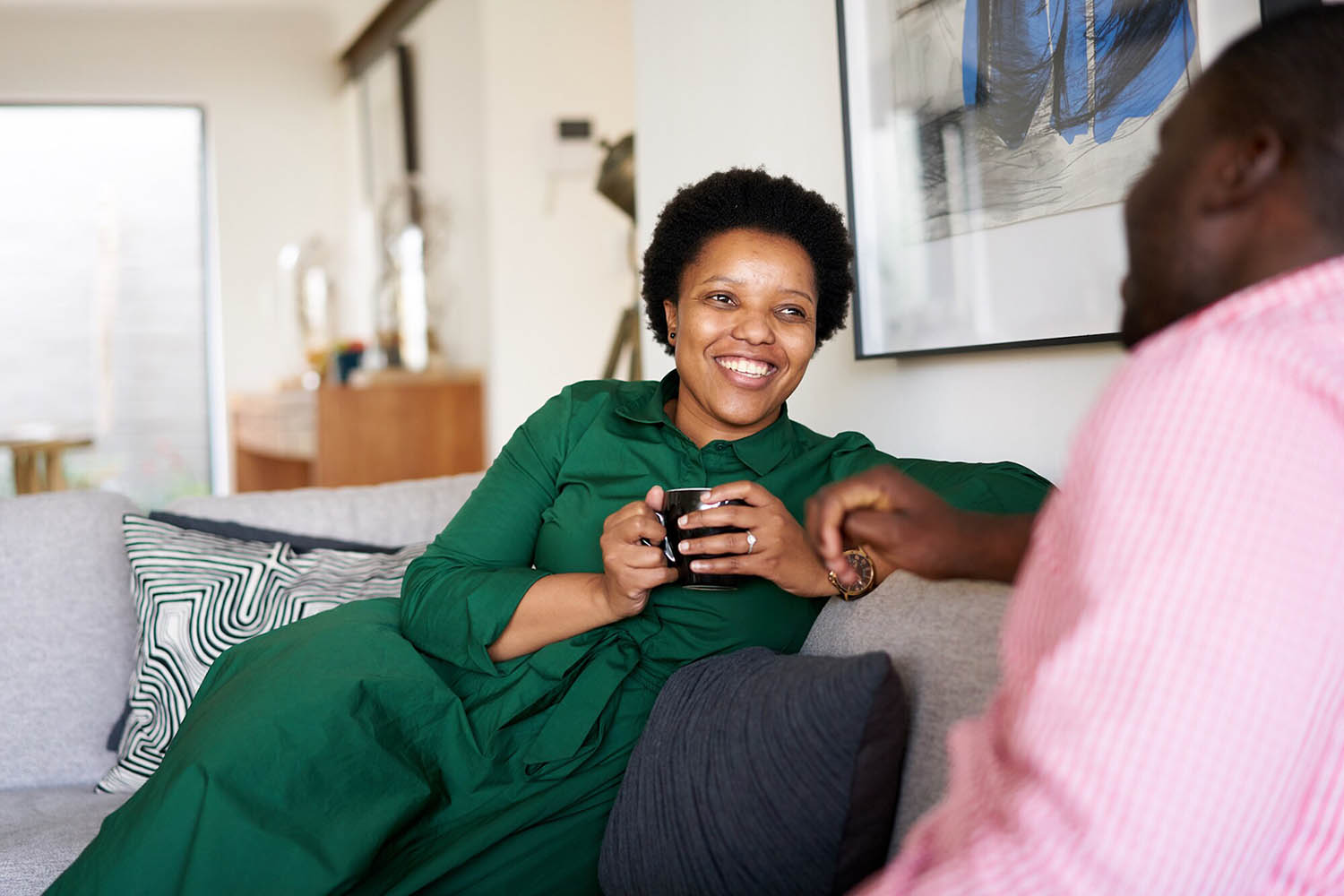 Lady smiling sat on sofa holding a mug