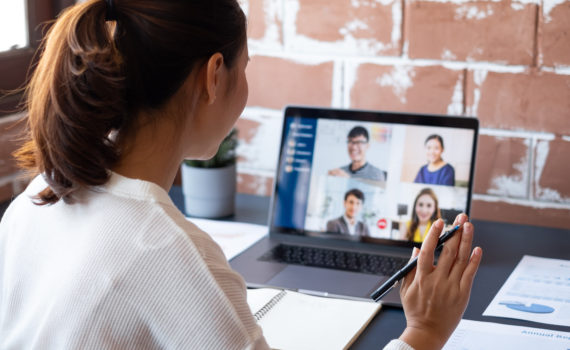 Young woman waving at screen of people in virtual meeting