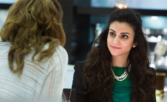 Wealth Management - Young woman with dark hair wearing a green shirt and a pearl necklace looking at person opposite her
