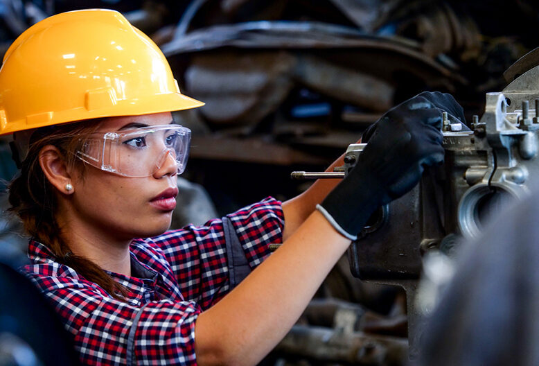 A woman in a hard hat works on machinery.