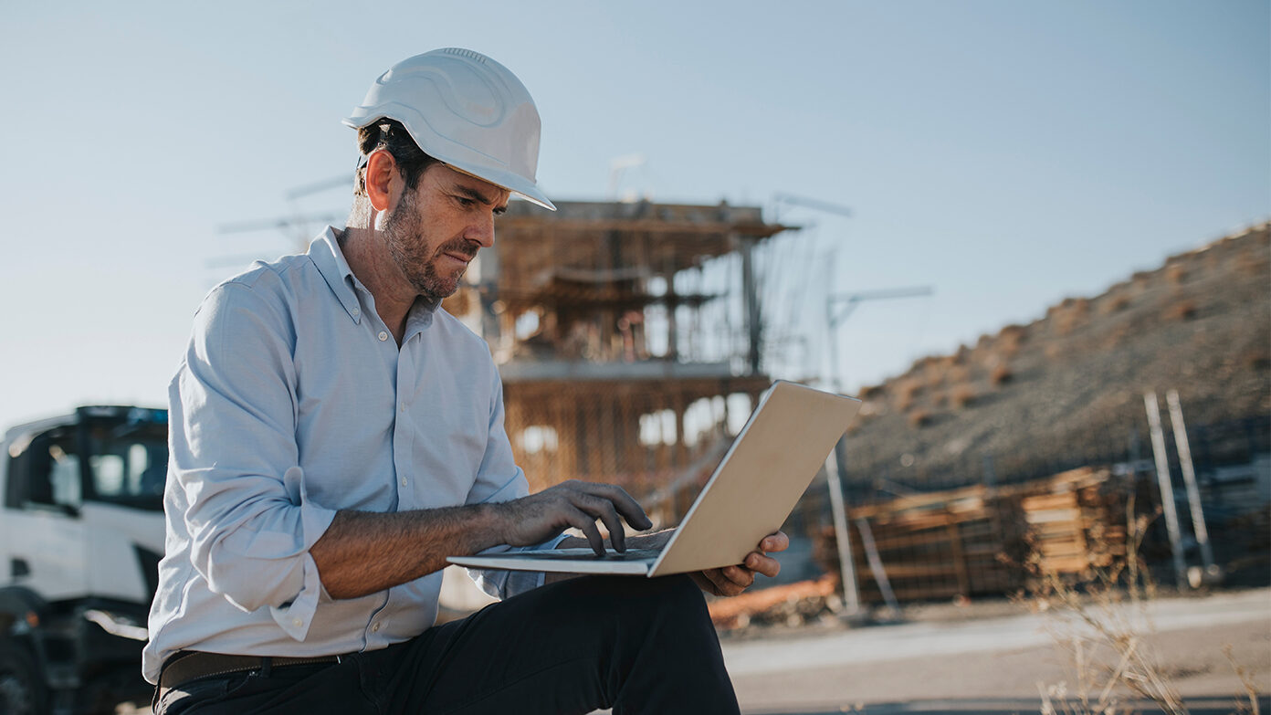 A man uses a laptop on a construction site.