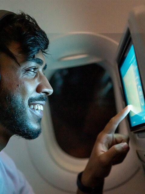 A passenger on a flight smiles as he uses a screen on a seat back.