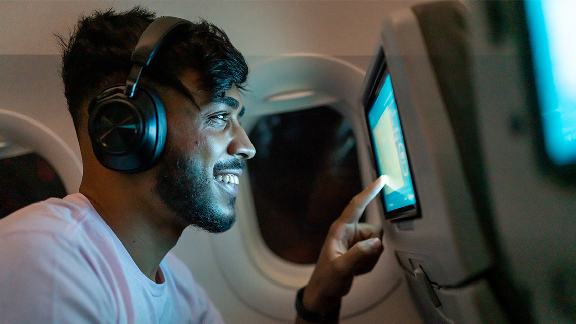 A passenger on a flight smiles as he uses a screen on a seat back.