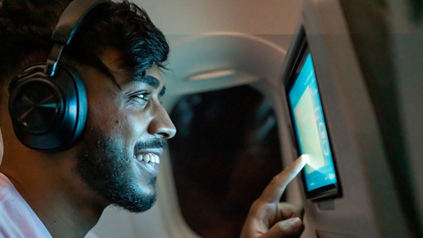 A passenger on a flight smiles as he uses a screen on a seat back
