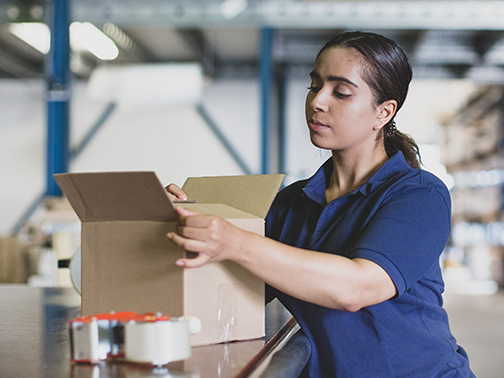 A woman packs a parcel in a warehouse.