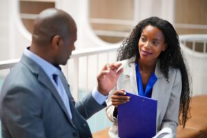 A woman with a clipboard gives information to a client in an office.