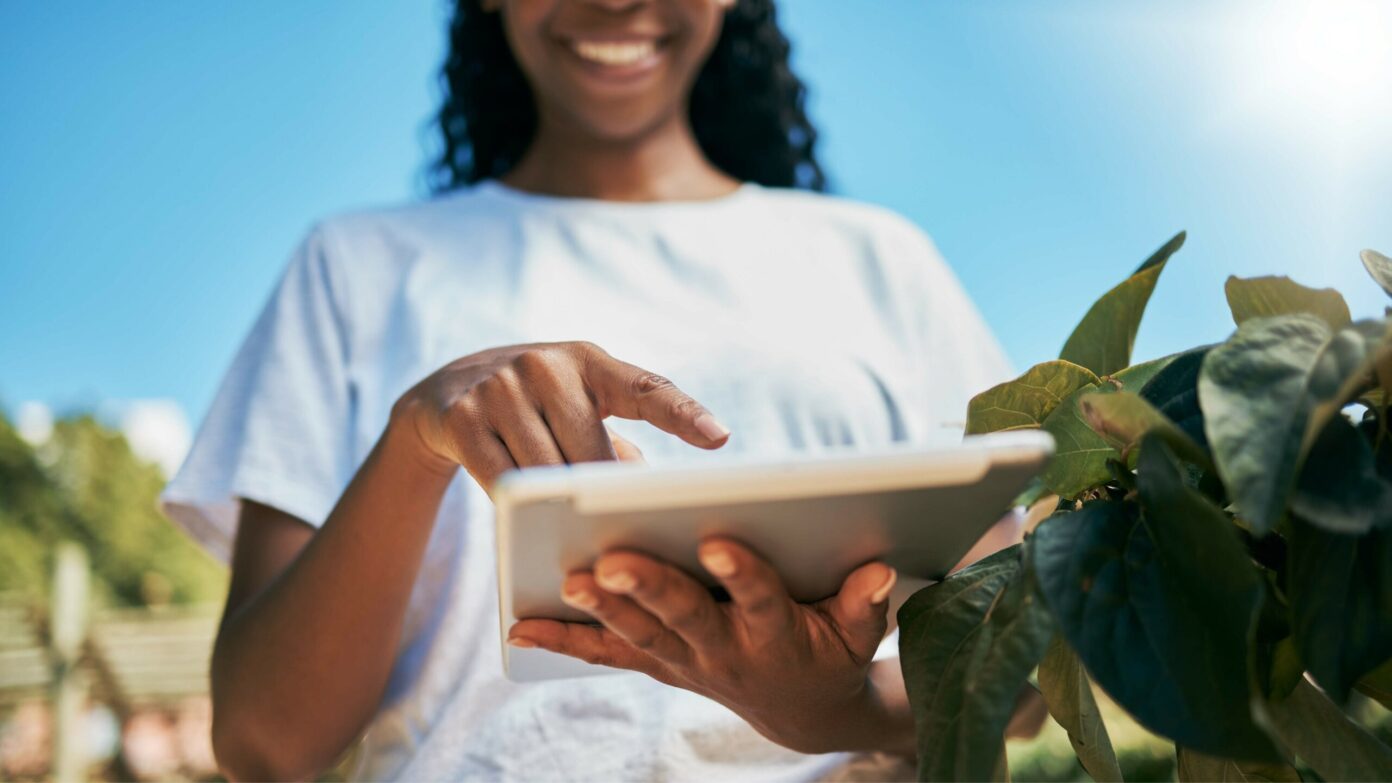 A young woman uses an iPad to assess crops.