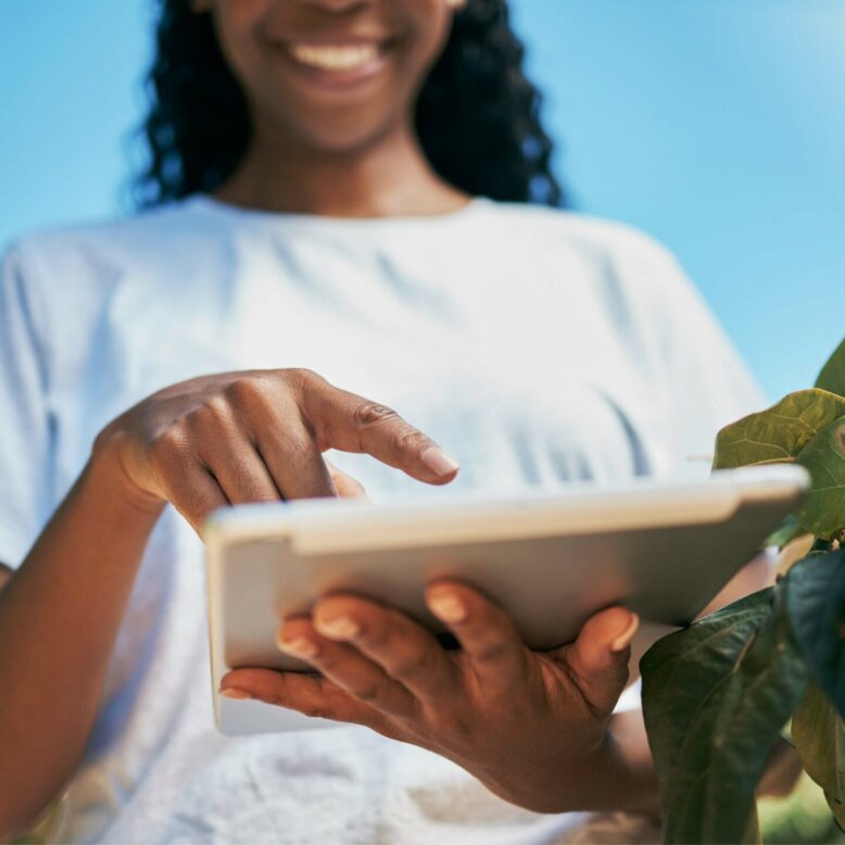 A young woman uses an iPad to assess crops.