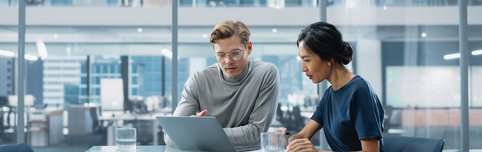 A man and a woman, in an office setup, looking at a laptop and discussing work