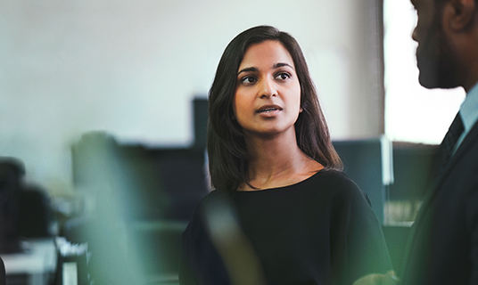 Two business people have a conversation in an office.