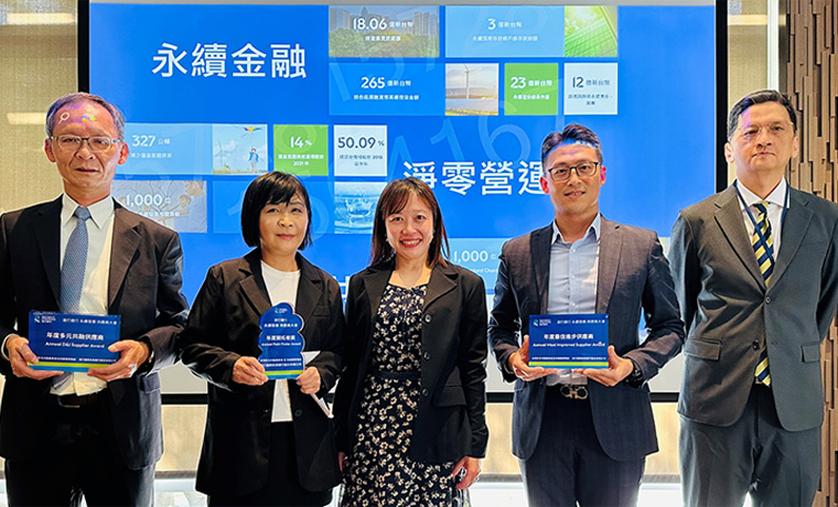 A diverse group of standard chartered colleagues smiling and posing together in front of a large screen.