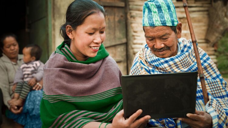 A woman shows a laptop to an elder in her rural community.