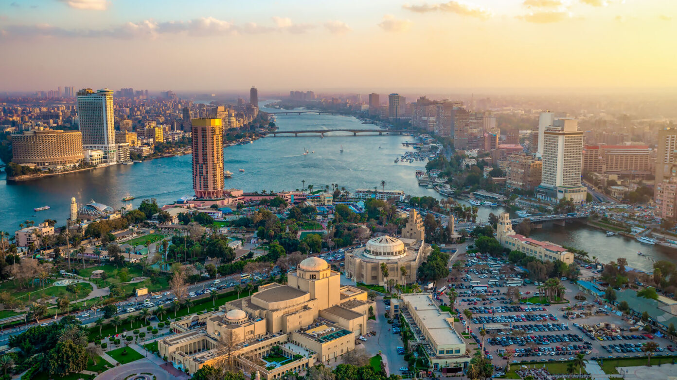 Aerial view of Cairo, Egypt, featuring the Nile river running through the city with prominent landmarks like Cairo Opera House and moden skyscrapers along the riverbank under the clear sky