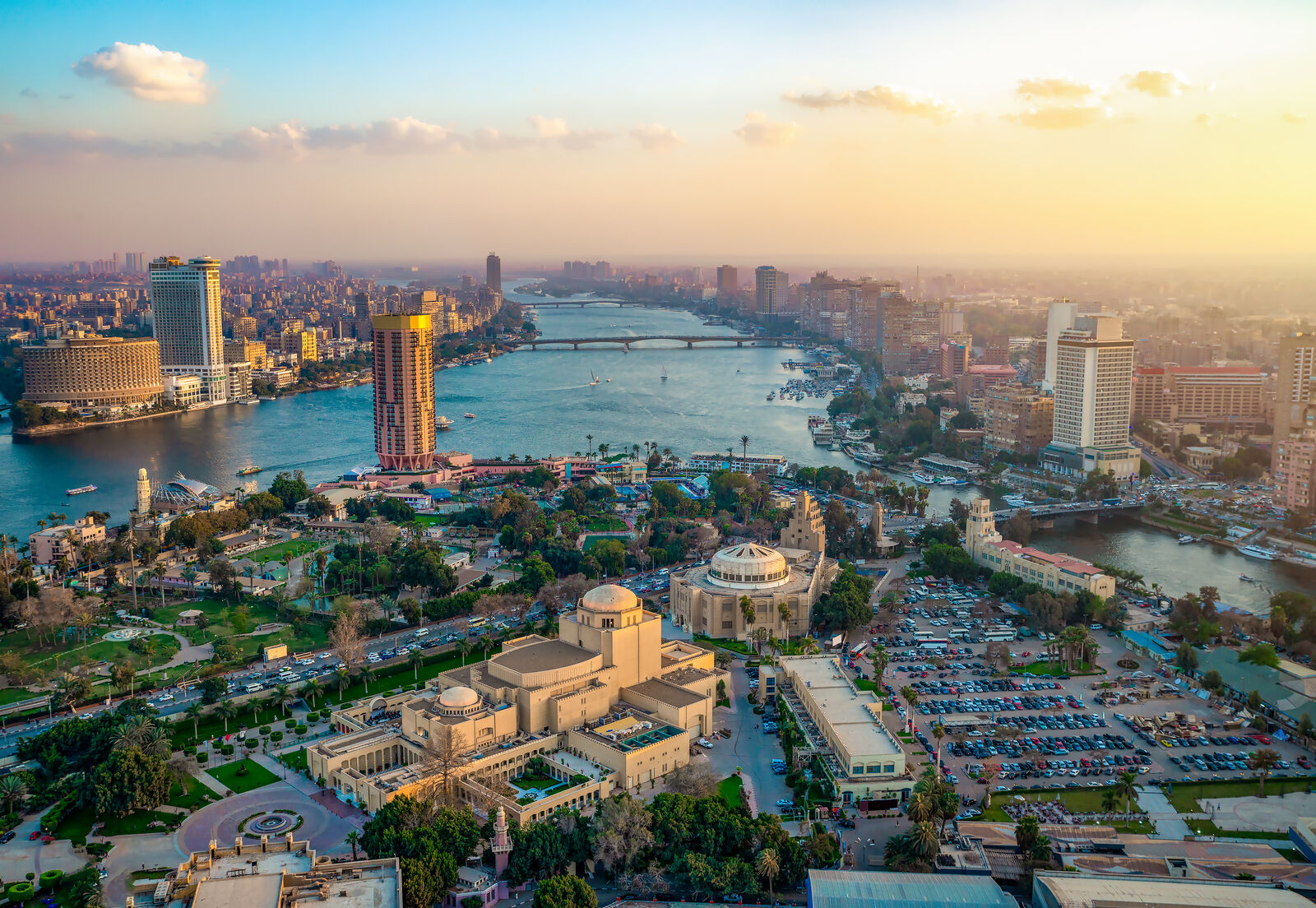 Aerial view of Cairo, Egypt, featuring the Nile river running through the city with prominent landmarks like Cairo Opera House and moden skyscrapers along the riverbank under the clear sky