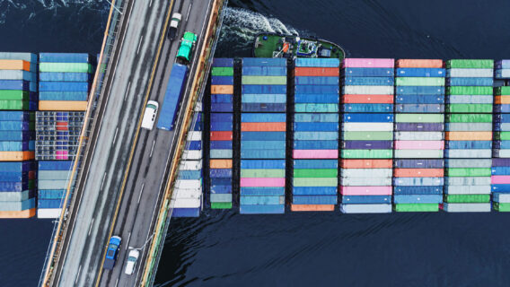 A highway over a river, where a container ship hauls cargo.