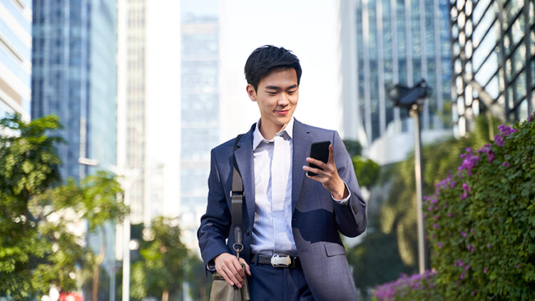 A man uses online banking on his phone while walking in a city.