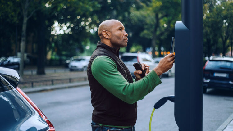 A man pays for a charge on an EV using a contactless card on mobile.