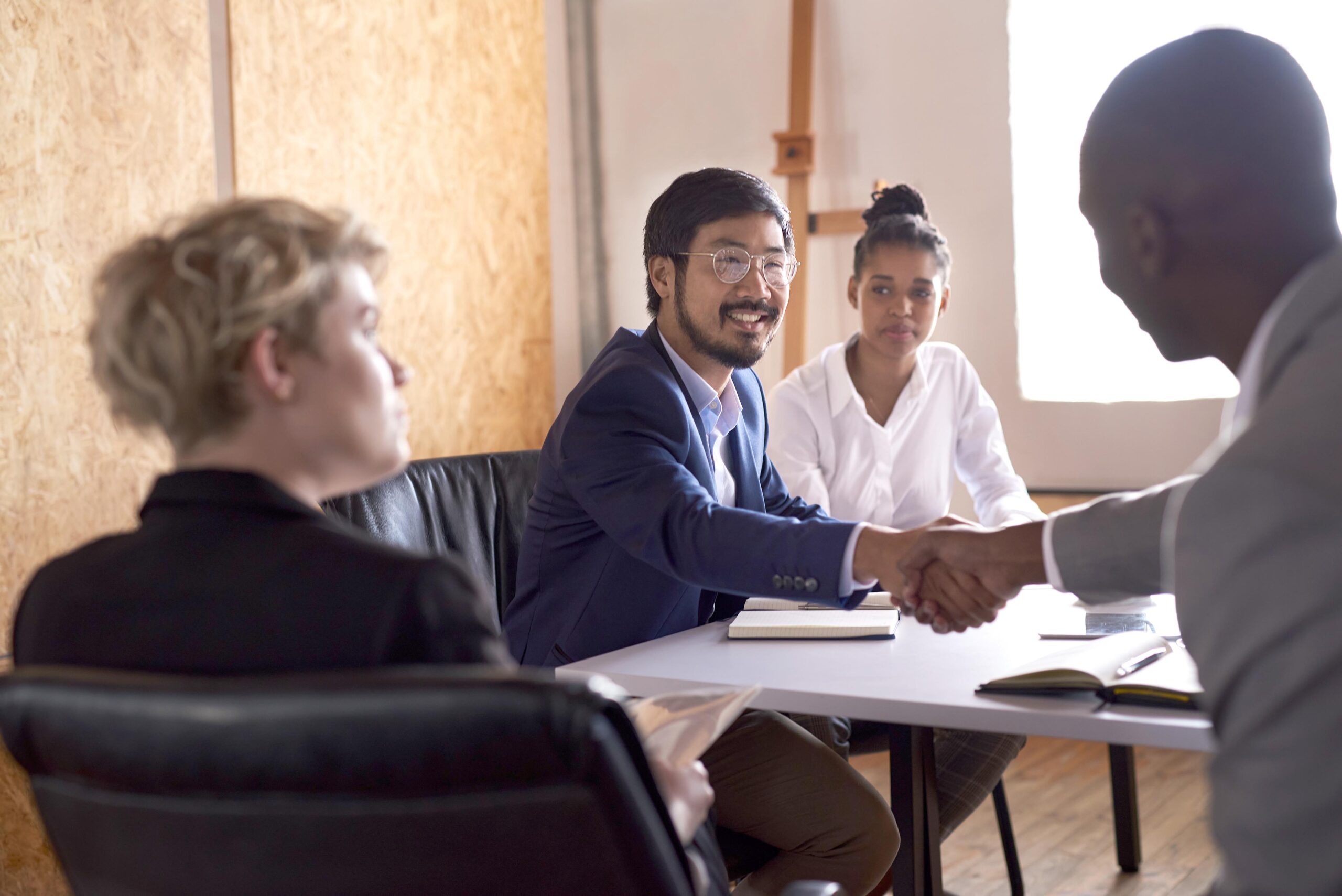 Smiling Asian businessman shaking hands with an African colleague during a meeting at a table in an office board room