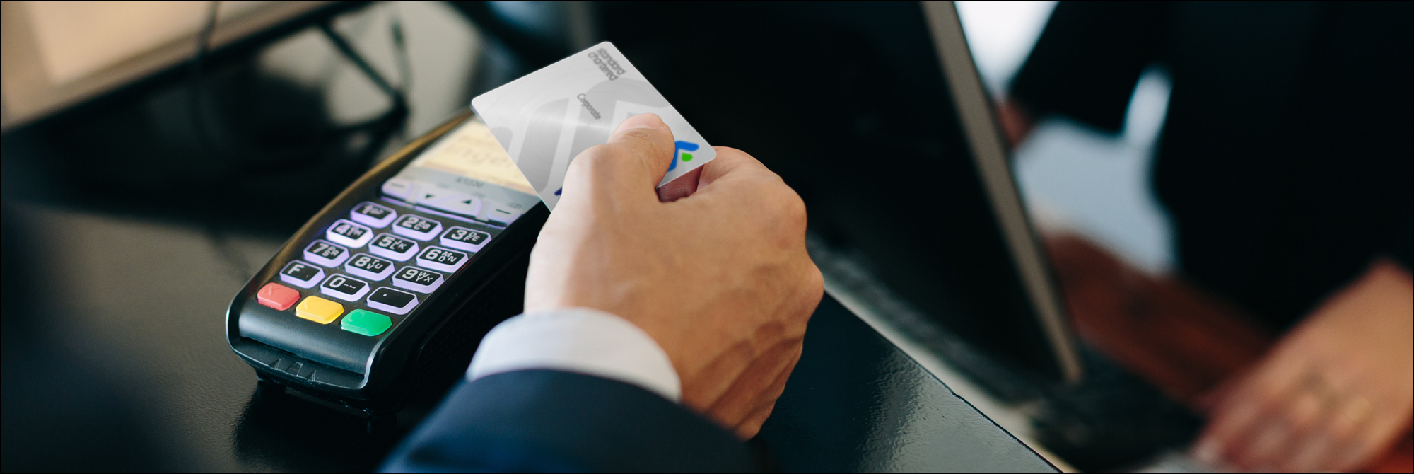 close up image of a hand holding a corporate credit card over a payment device