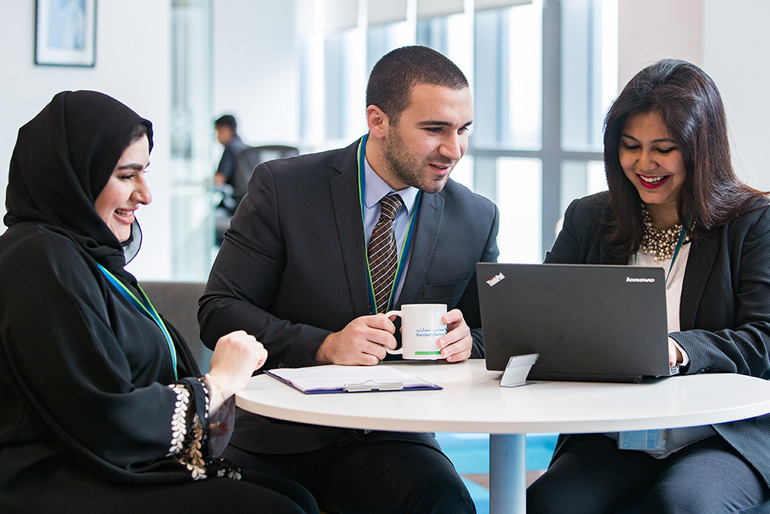 Three employees smiling and looking at a laptop in a casual meeting