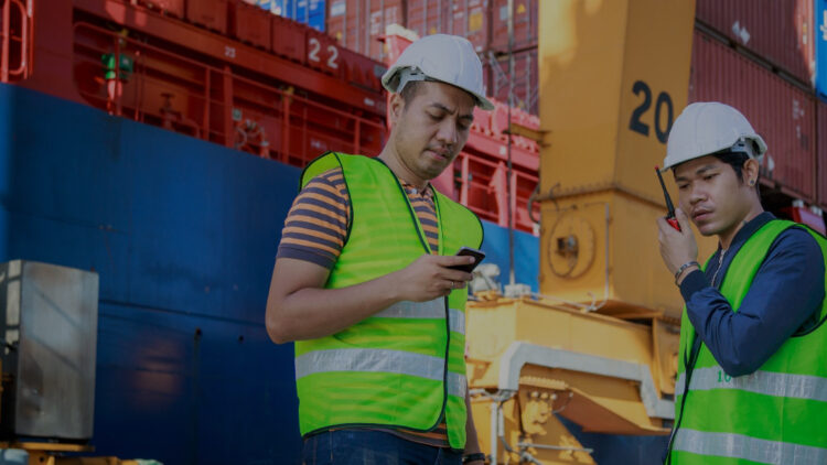 Two men wearing high-vis working near shipping containers