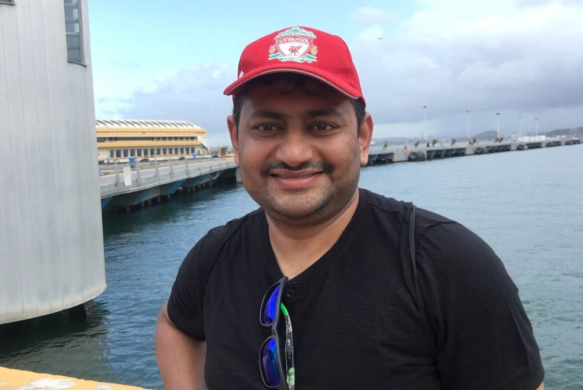 Tanmay Sahay standing in front of lake wearing a red cap