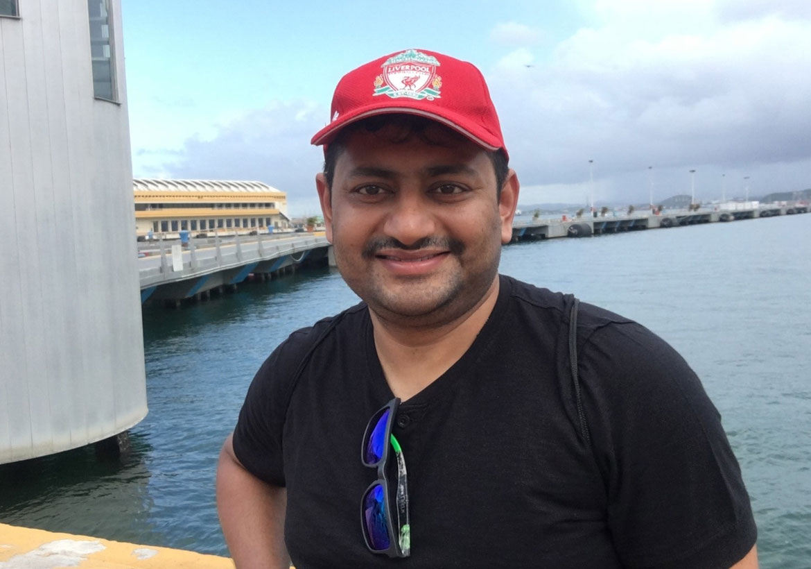 Tanmay Sahay standing in front of lake wearing a red cap