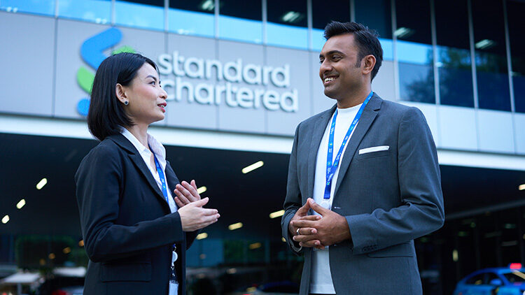 Two experienced career professionals chat together outside a Standard Chartered office in Singapore.