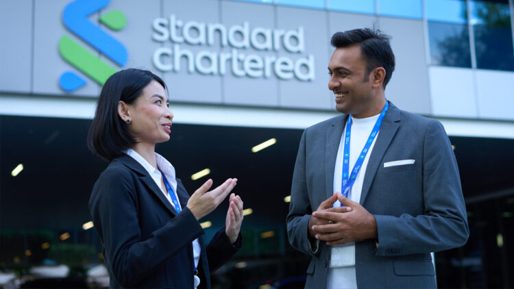 Two colleagues have a conversation outside a Standard Chartered office.
