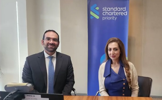 Two Standard Chartered colleagues smile behind a table.