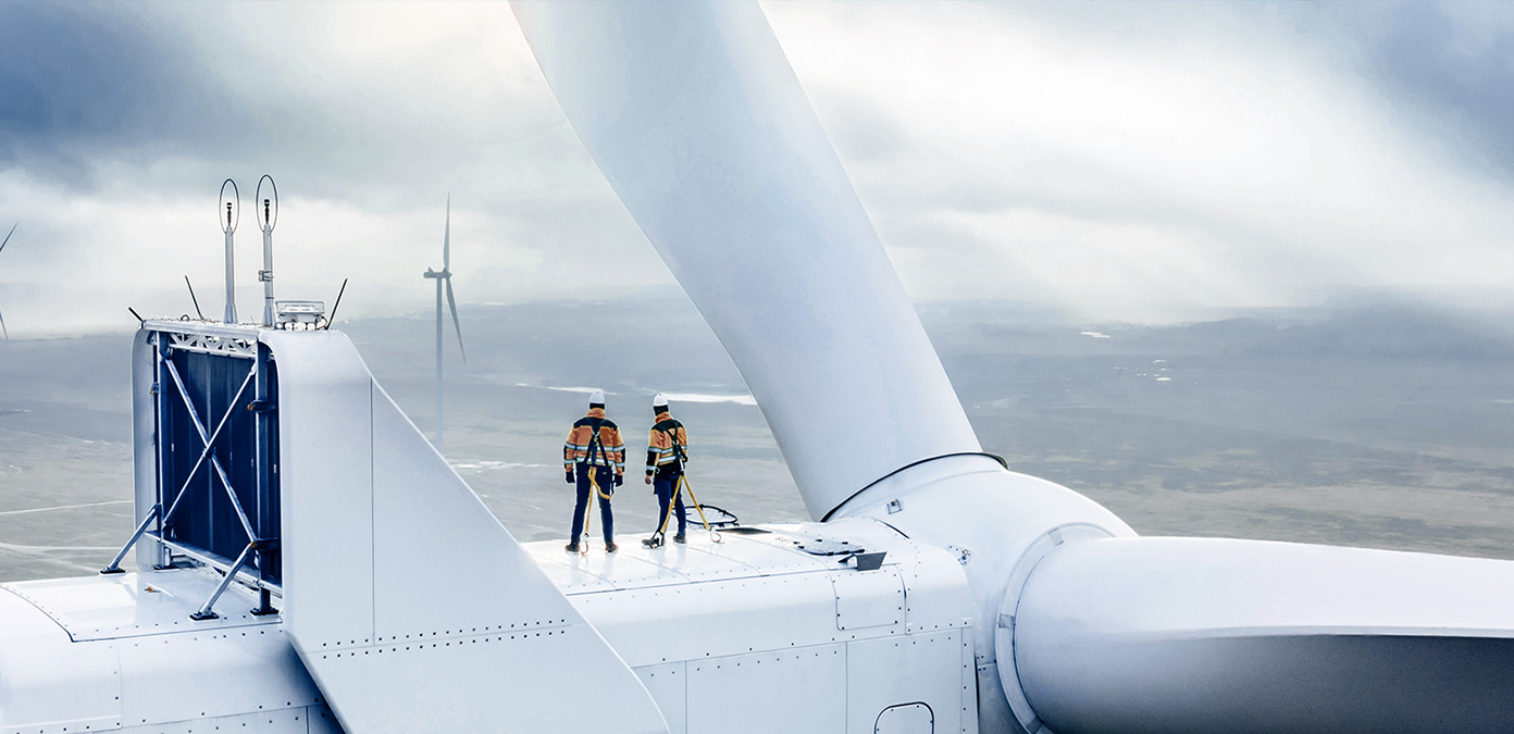 Two workers stand on a wind turbine.