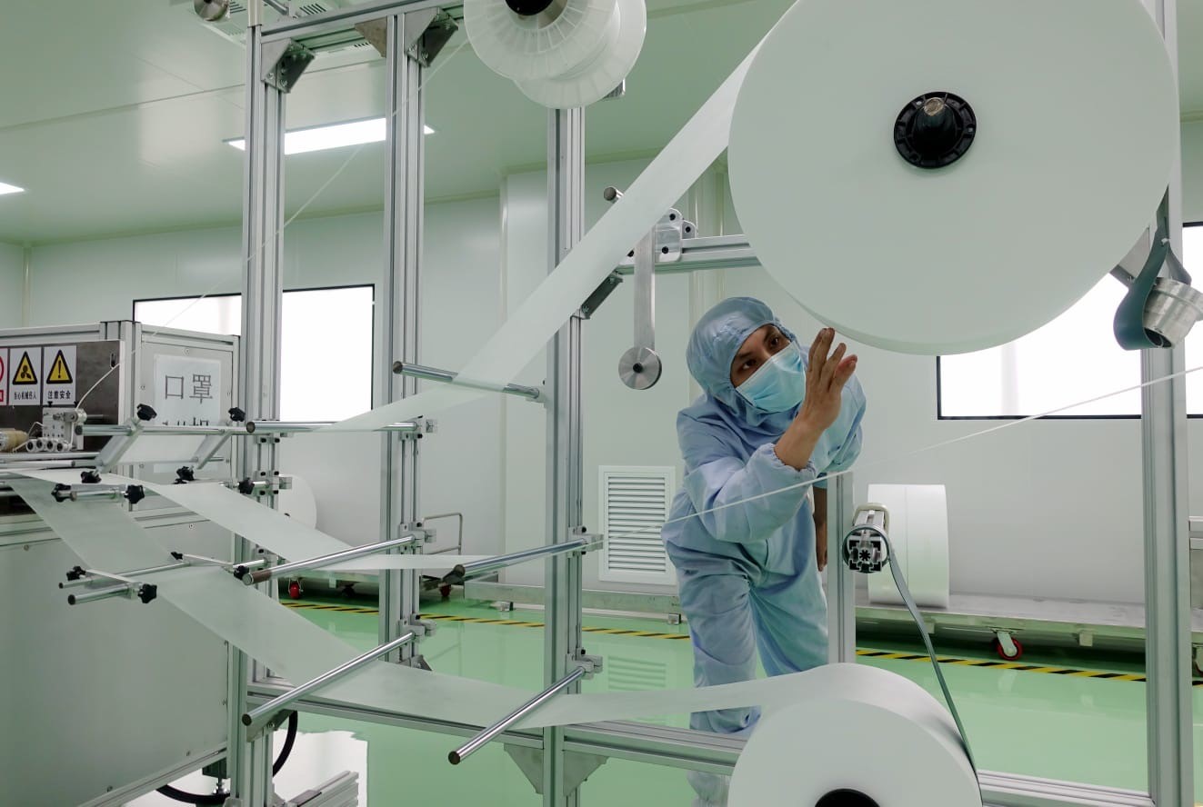 person in face mask and hair net inspecting machine