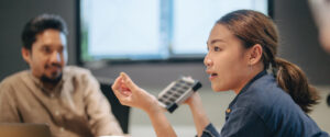 A young woman presents a model solar panel to a meeting room of colleagues.