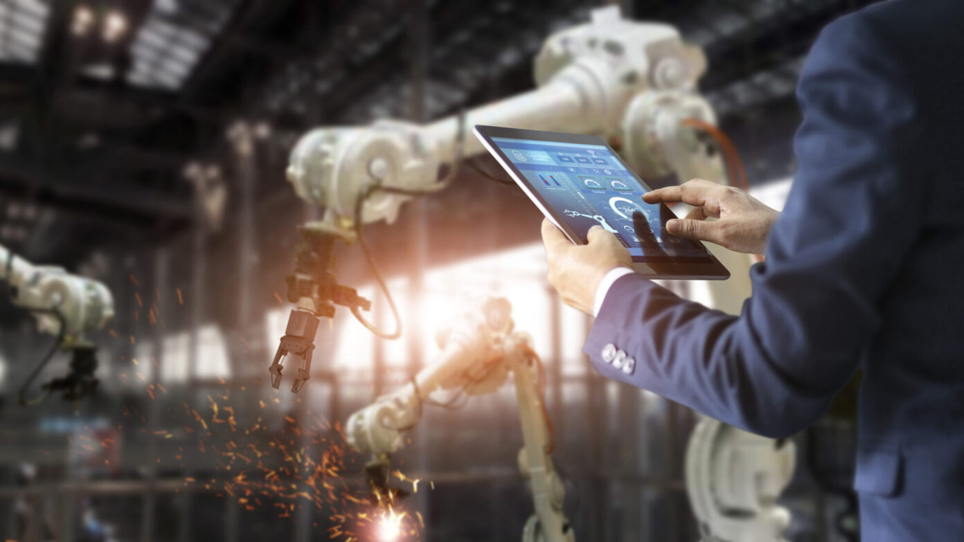 A man with an ipad in a factory operating a robot