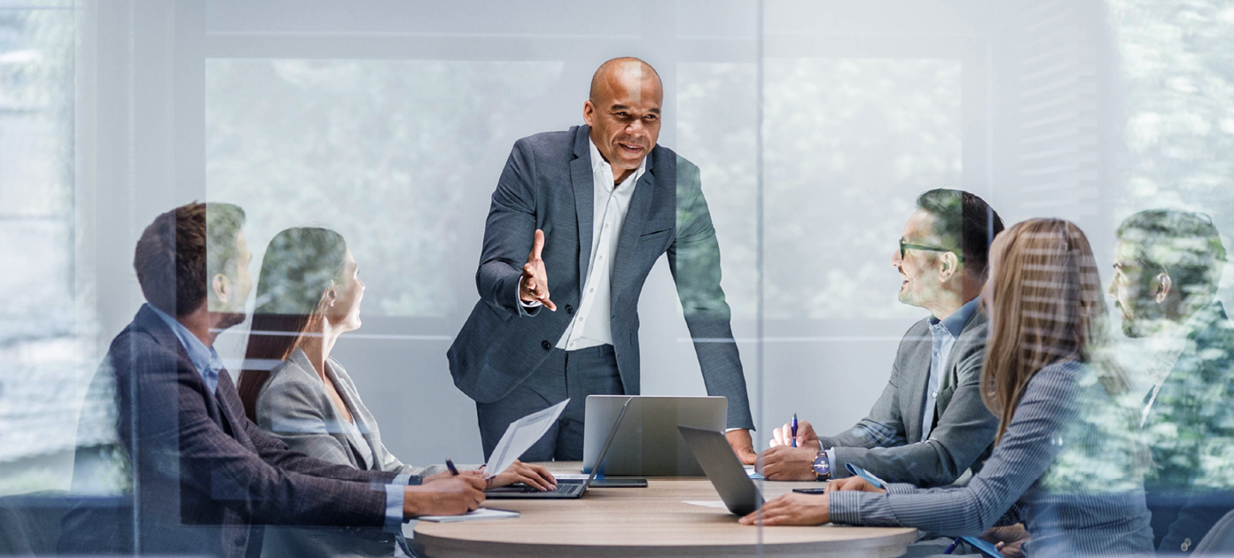 Man giving a presentation with laptop on the table for 5 people inside a meeting room