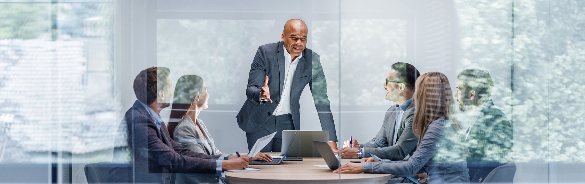 Man giving a presentation with laptop on the table for 5 people inside a meeting room