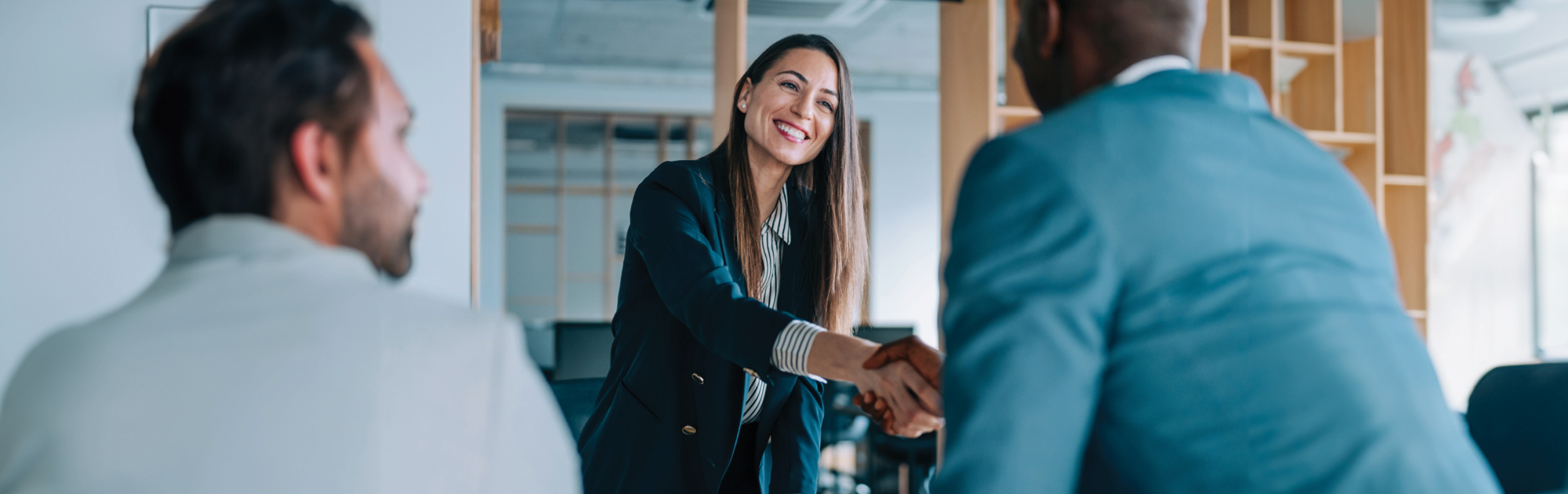 A woman in a suit smiles as she gives a hand shake to a man