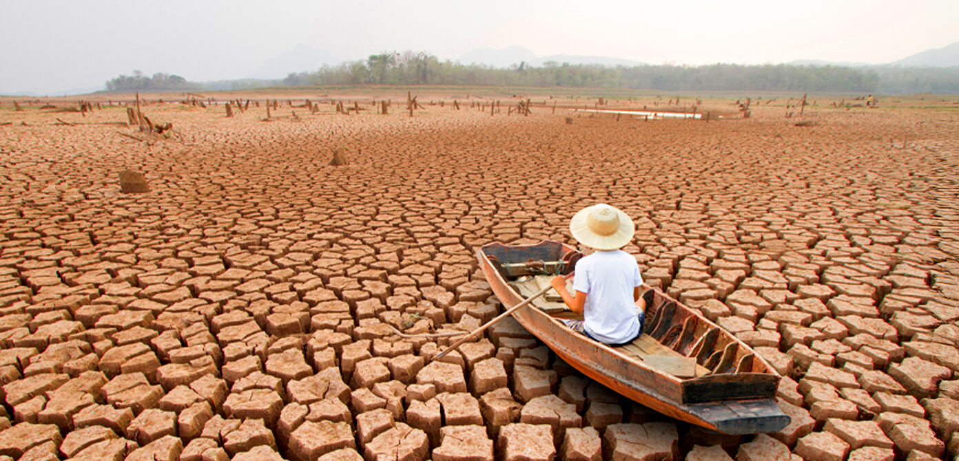 A man on a wooden boat, in the middle of a dry arid land