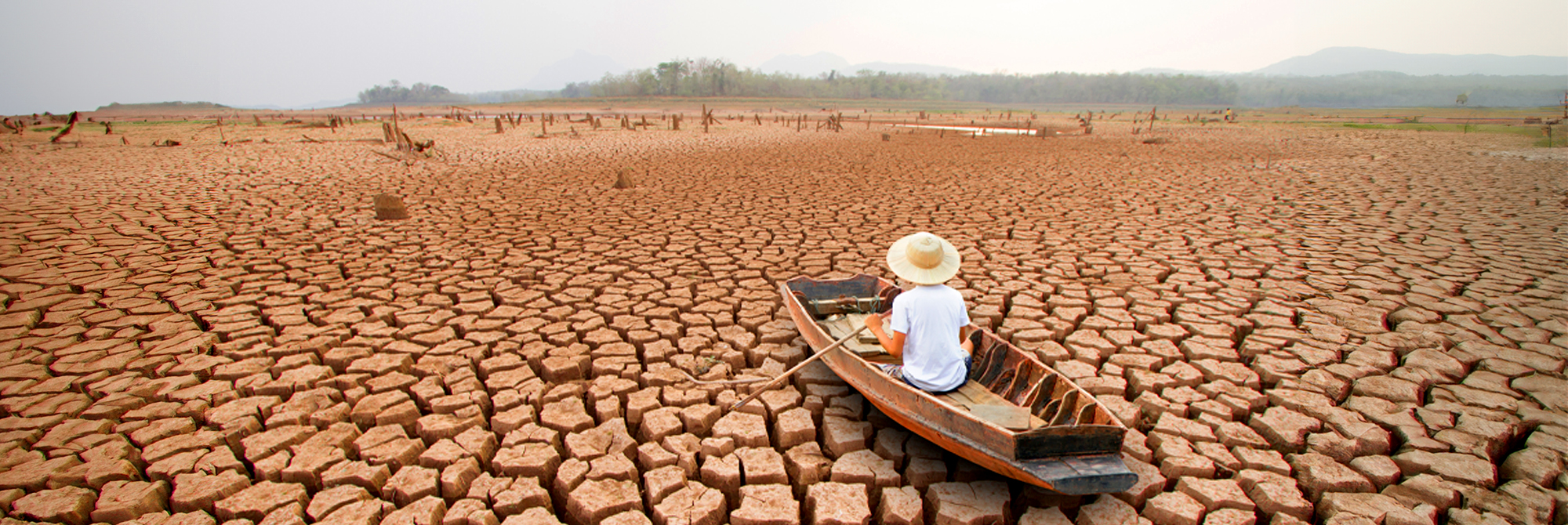 A man on a wooden boat, in the middle of a dry arid land