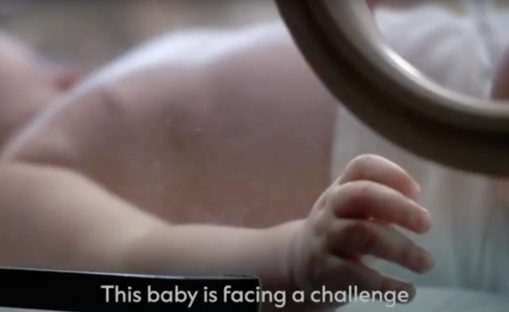 A still from the video shows a baby in an incubator.