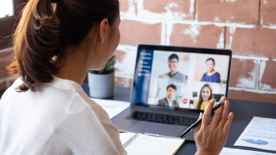 Young woman waving at screen of people in virtual meeting