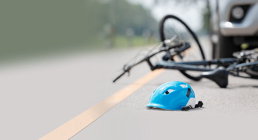 A bike and a light blue cycling helmet falling on the road, with a car in the background